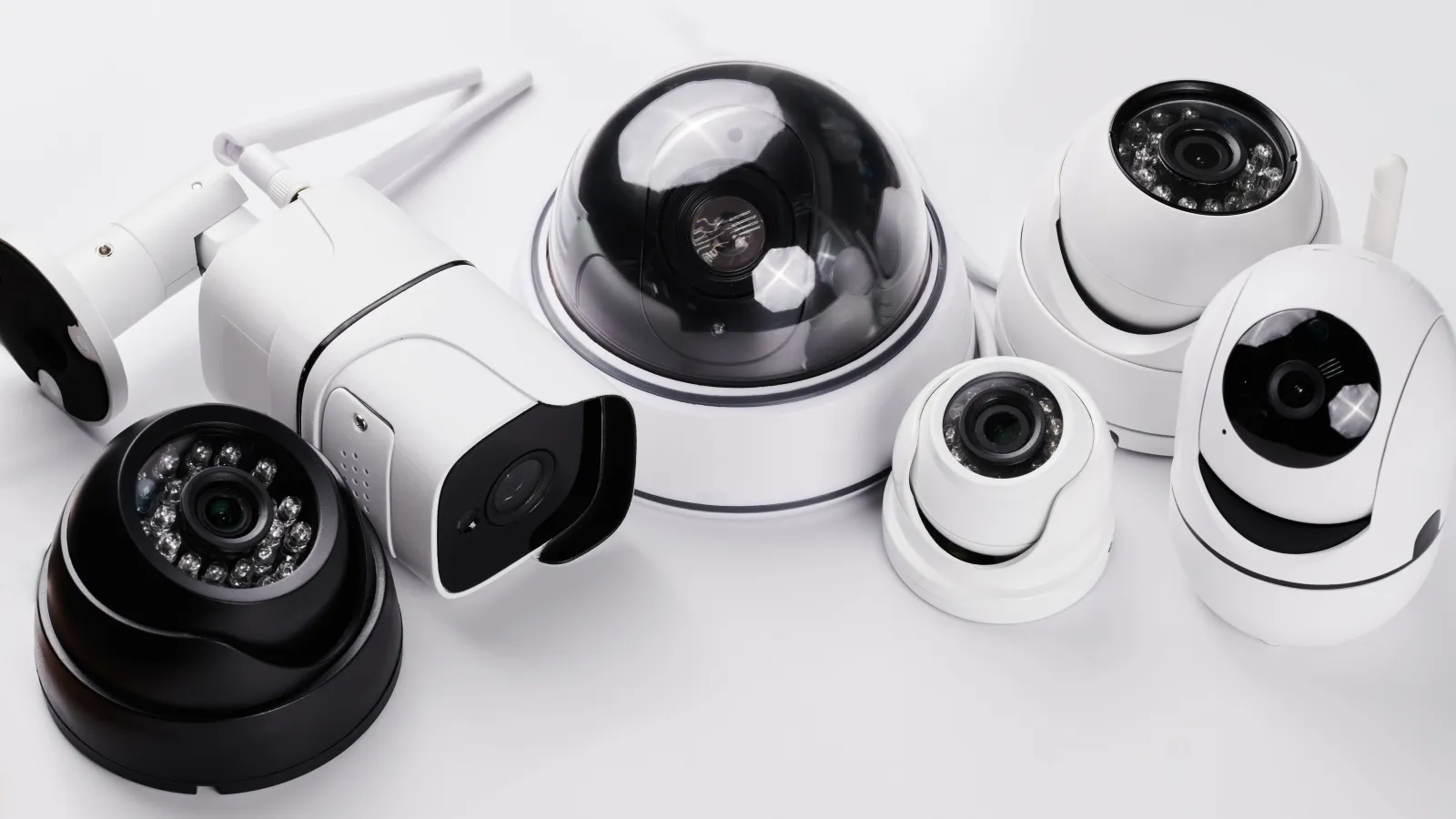 Variety of white and black security cameras on a white surface showing multiple models and designs.