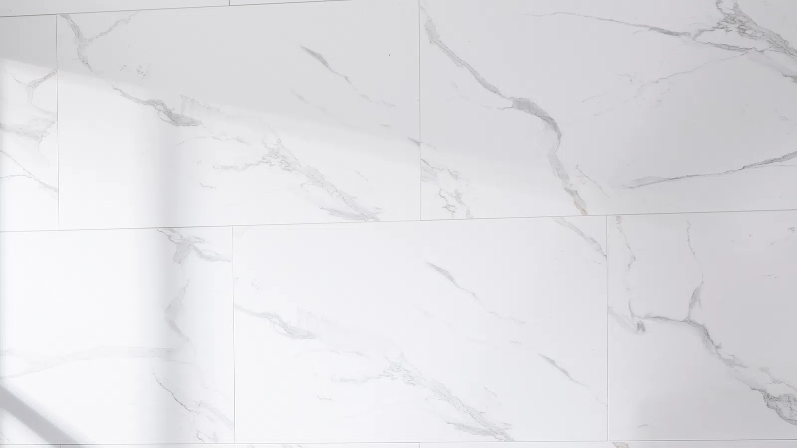 White marble tiles with gray veining arranged in a staggered pattern on a smooth surface.