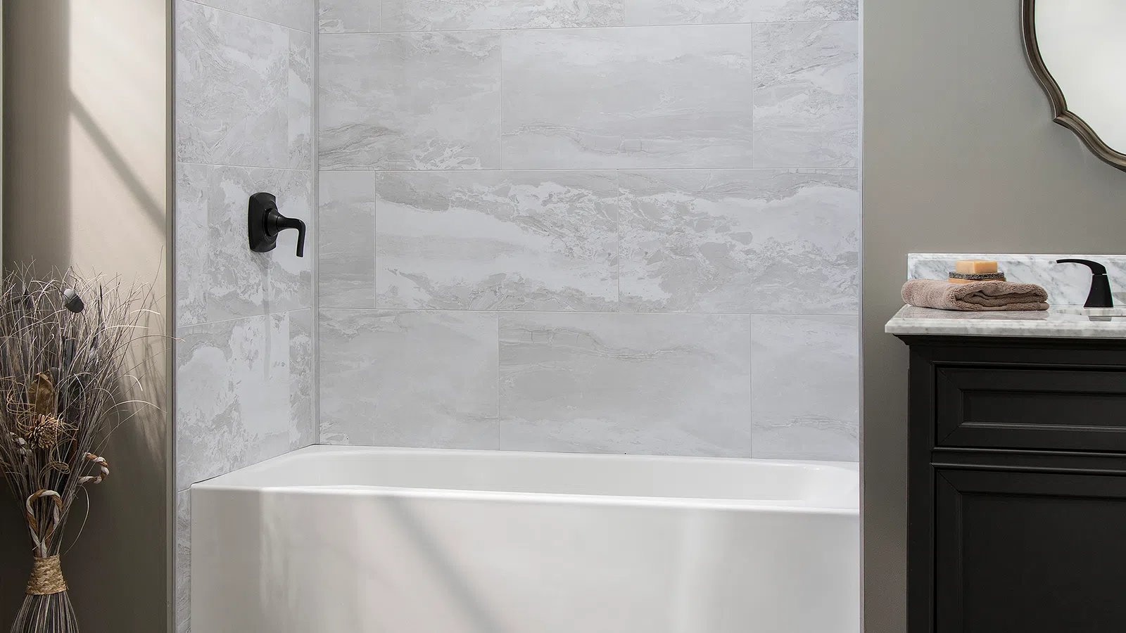 Modern bathroom with white bathtub, gray marble tile shower, black fixtures, and dark vanity with mirror.