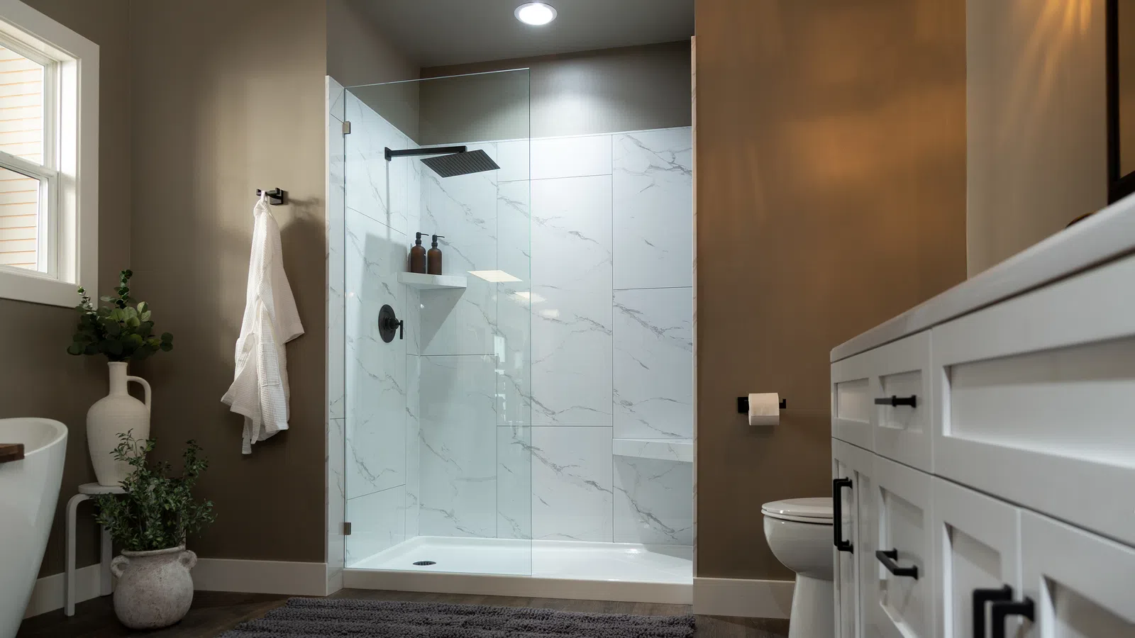 Modern bathroom with glass shower enclosure, white marble tiles, dark wood floor, white vanity, and plants.