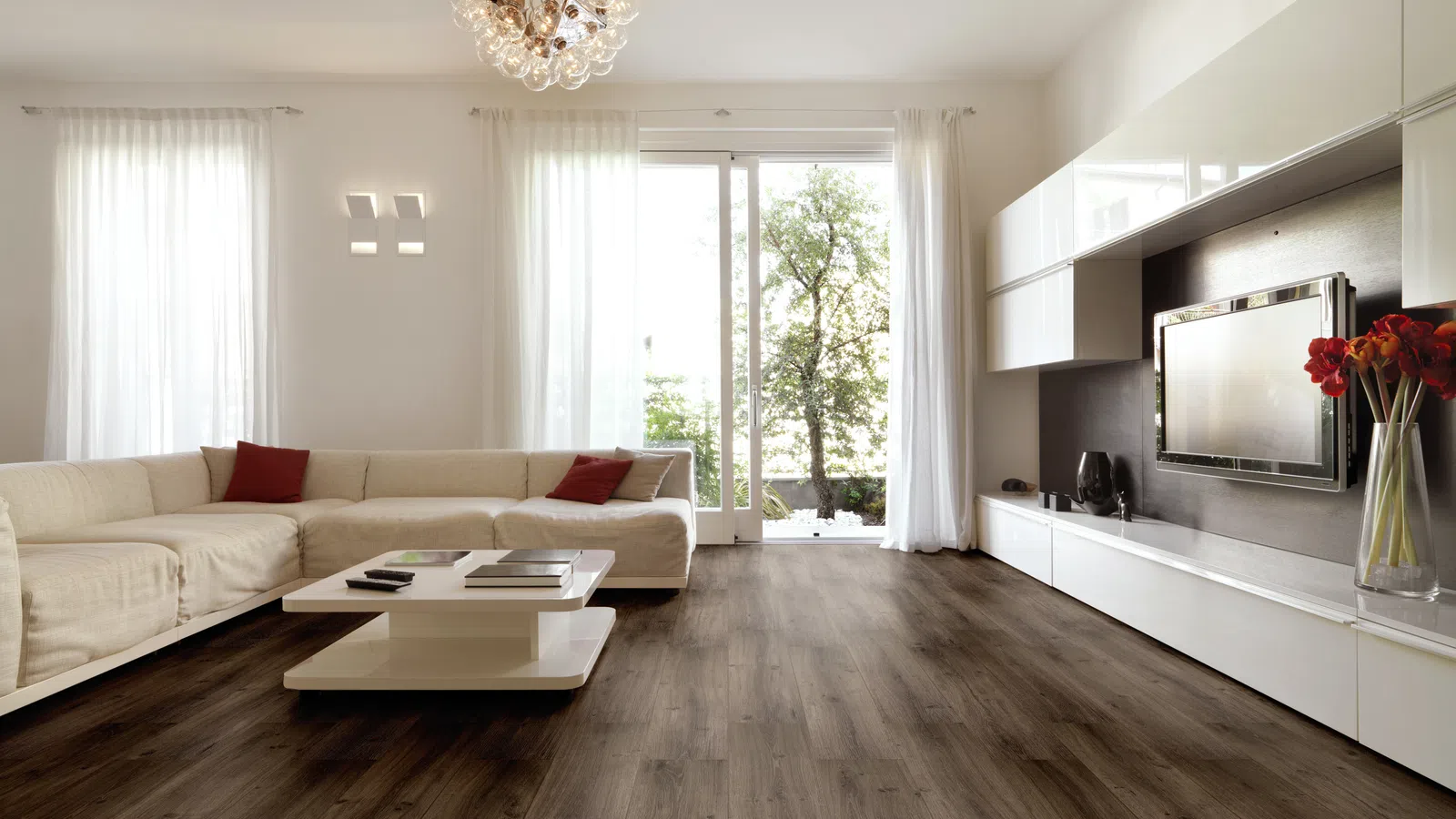 Bright modern living room with white sectional sofa, dark wood floor, glass coffee table, and large window.