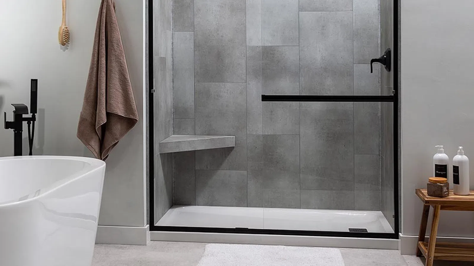 Modern shower corner with dark gray tiles, built-in shelves holding bottles and scrub, and a black handheld showerhead.