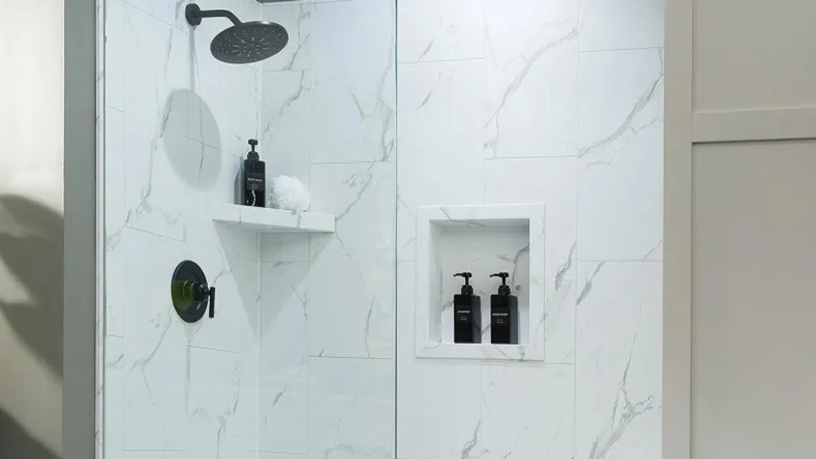 Modern white marble bathroom shower with rain showerhead and built-in shelves beside a large potted plant.