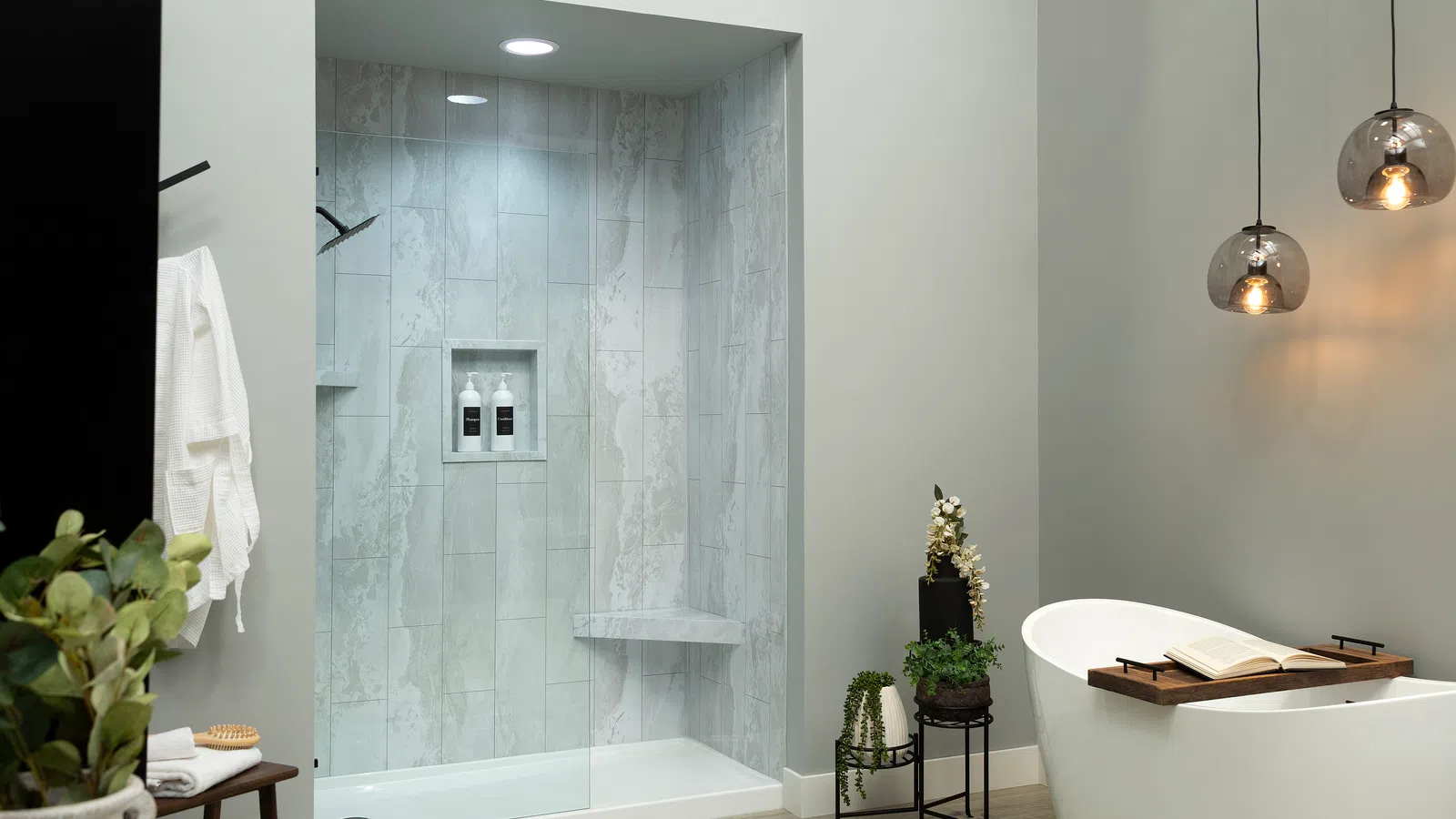 Modern bathroom with marble tiled shower, freestanding bathtub, hanging lights, and decorative plants.