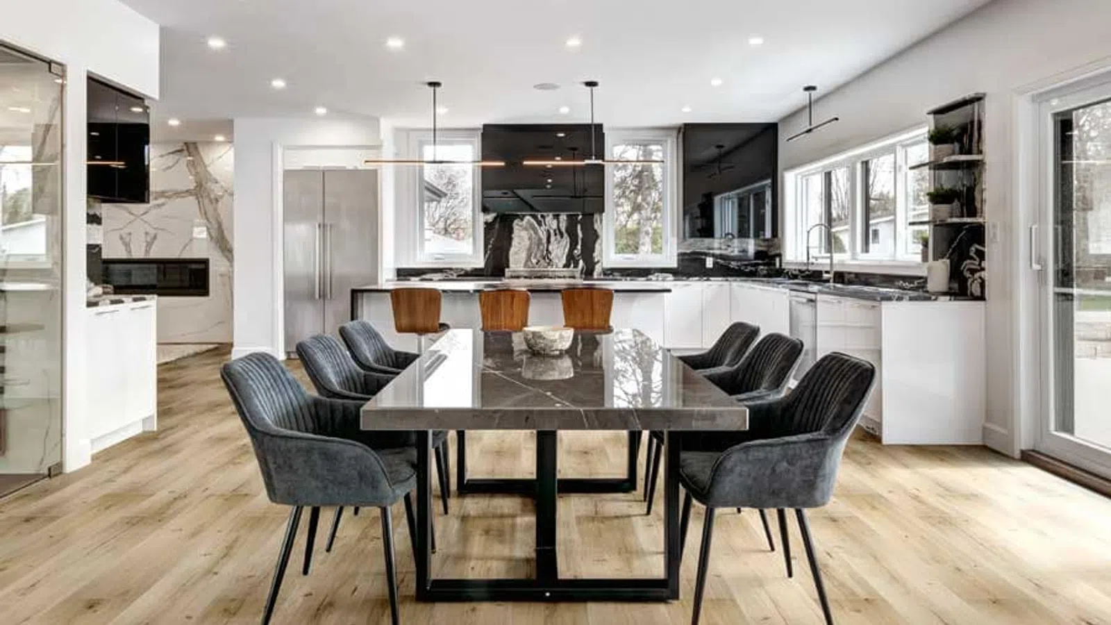 Modern kitchen and dining area with wooden flooring, black marble table, gray chairs, and white cabinetry.