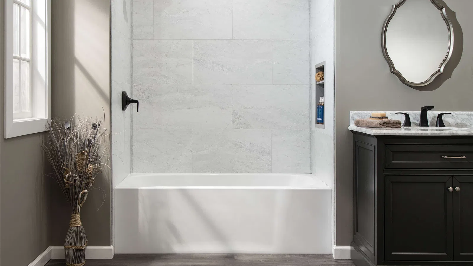 Modern bathroom with white bathtub, dark wood vanity, decorative mirror, and wood-look flooring under natural light.