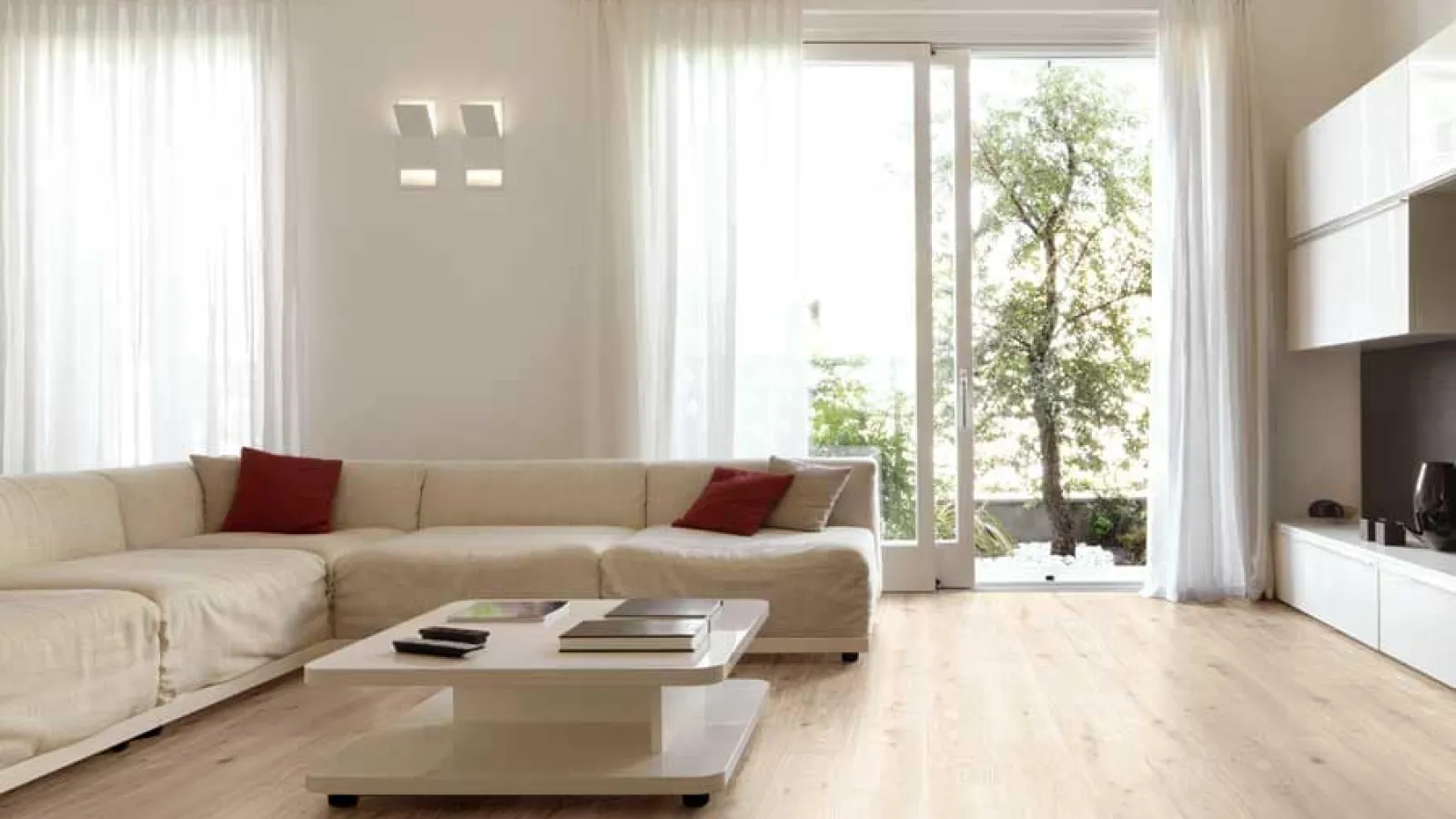 Bright modern living room with beige sectional sofa, white coffee table, chandelier, and large glass doors to garden.