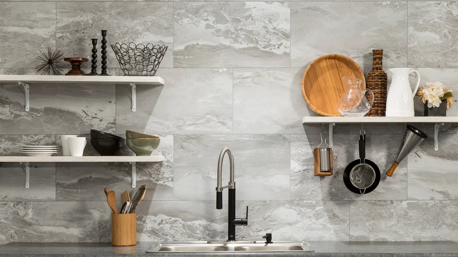 Modern kitchen with gray marble tile backsplash, stainless steel sink, wooden utensils, and open shelves with decor.