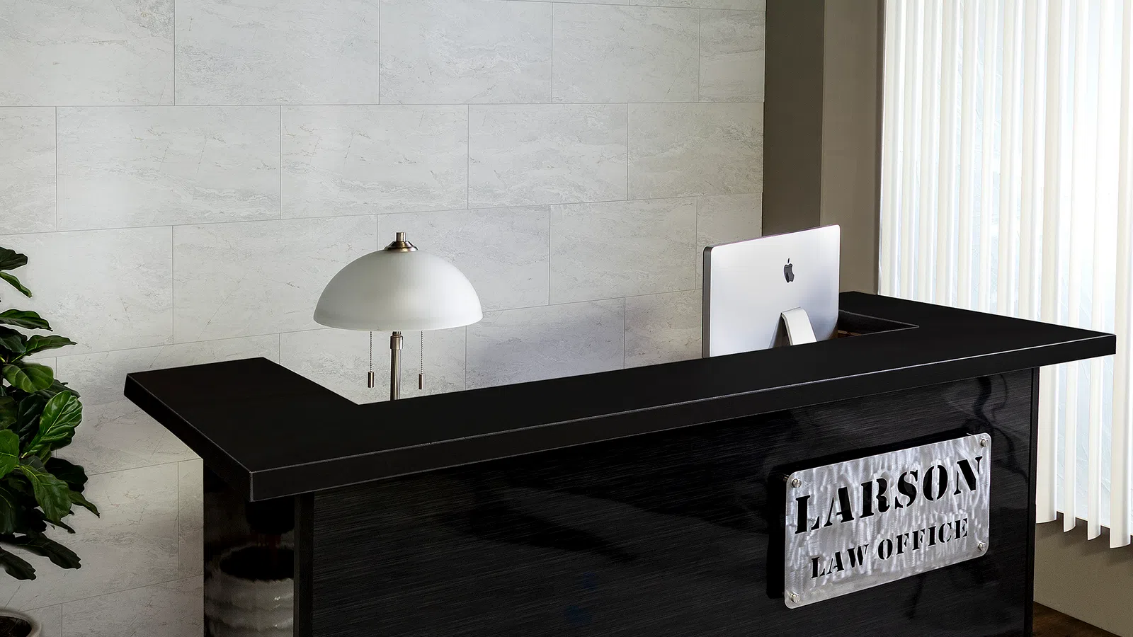 Modern law office reception with black desk, Larson Law Office sign, desk lamp, computer, and window blinds.