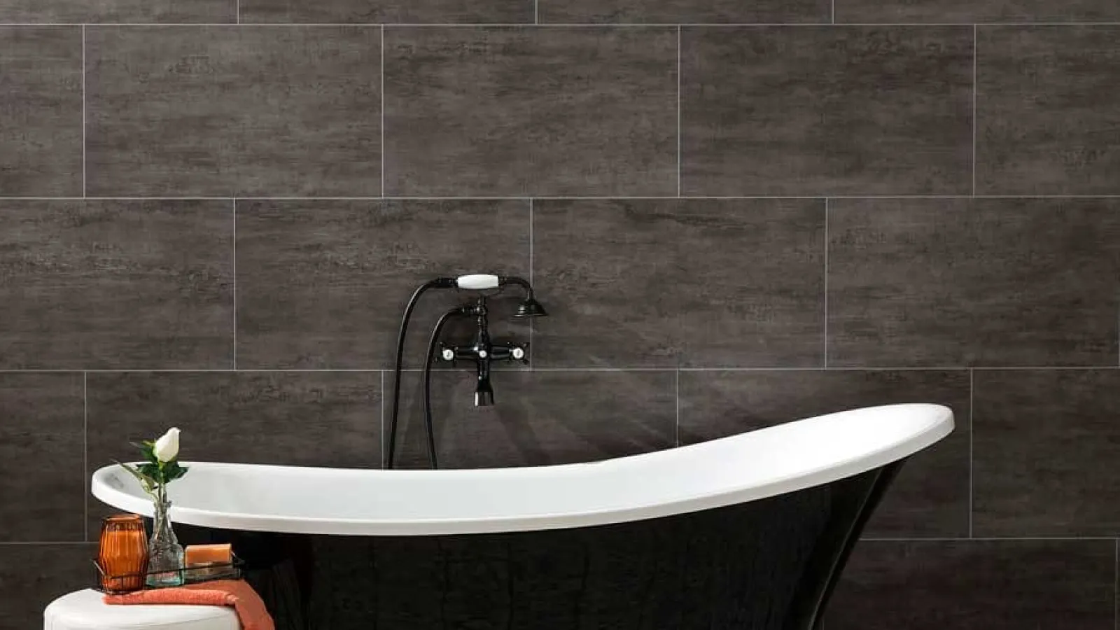 Modern black clawfoot bathtub with silver feet against dark tiled wall and patterned floor tiles.