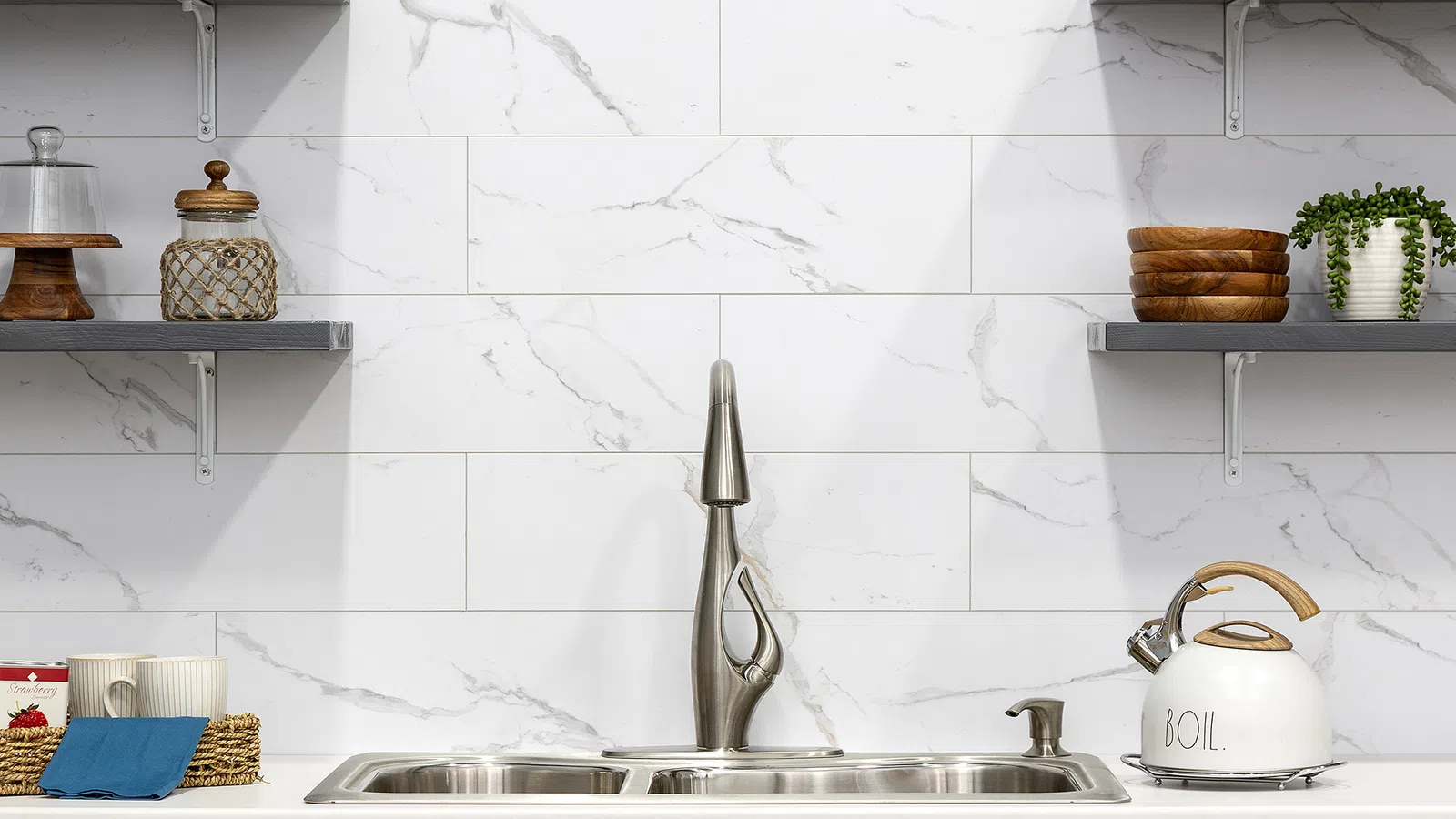 Modern kitchen sink with stainless steel faucet, marble backsplash, dark wood cabinets, and open shelves with decor.
