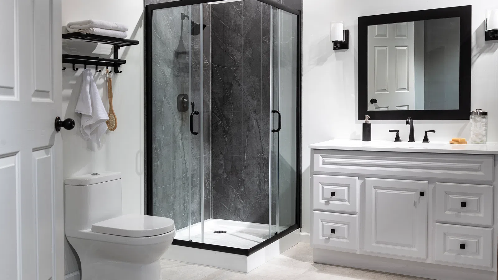 Modern bathroom with glass shower, white vanity, black fixtures, toilet, mirror, and towel rack.