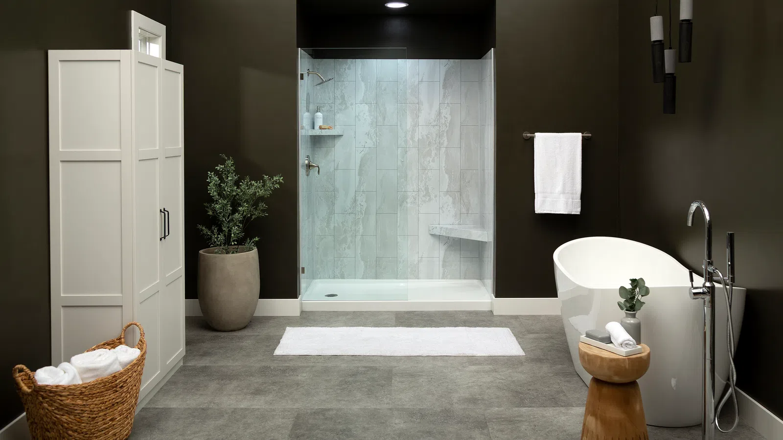 Modern bathroom with glass shower, freestanding bathtub, white towels, large plant, and dark walls.