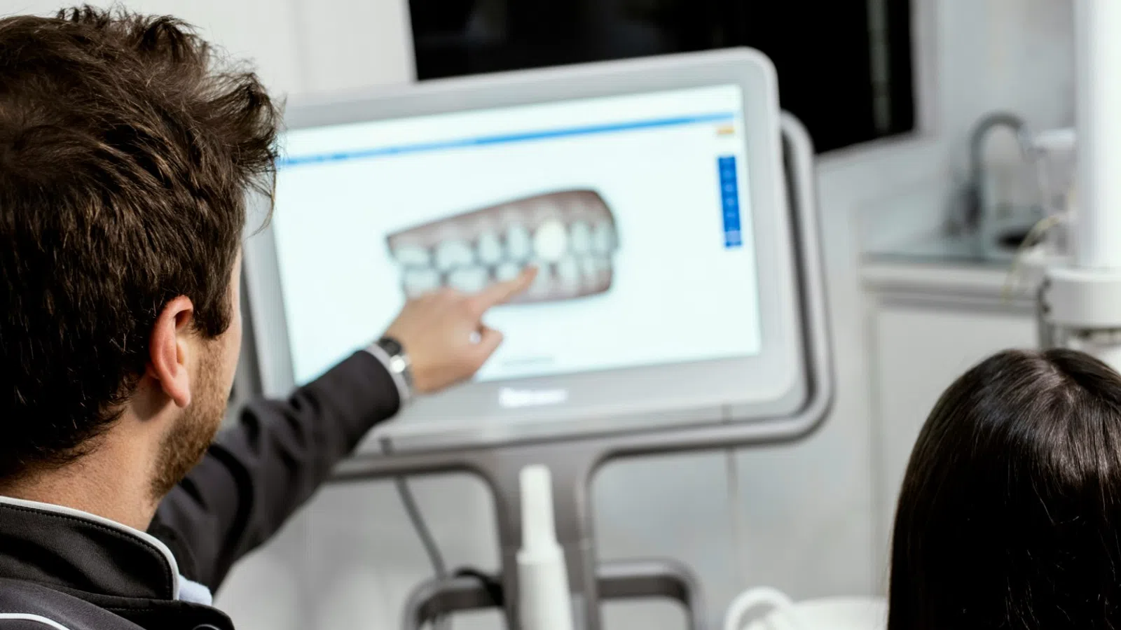 Dentist explaining dental X-ray on screen to patient sitting in dental chair during consultation.