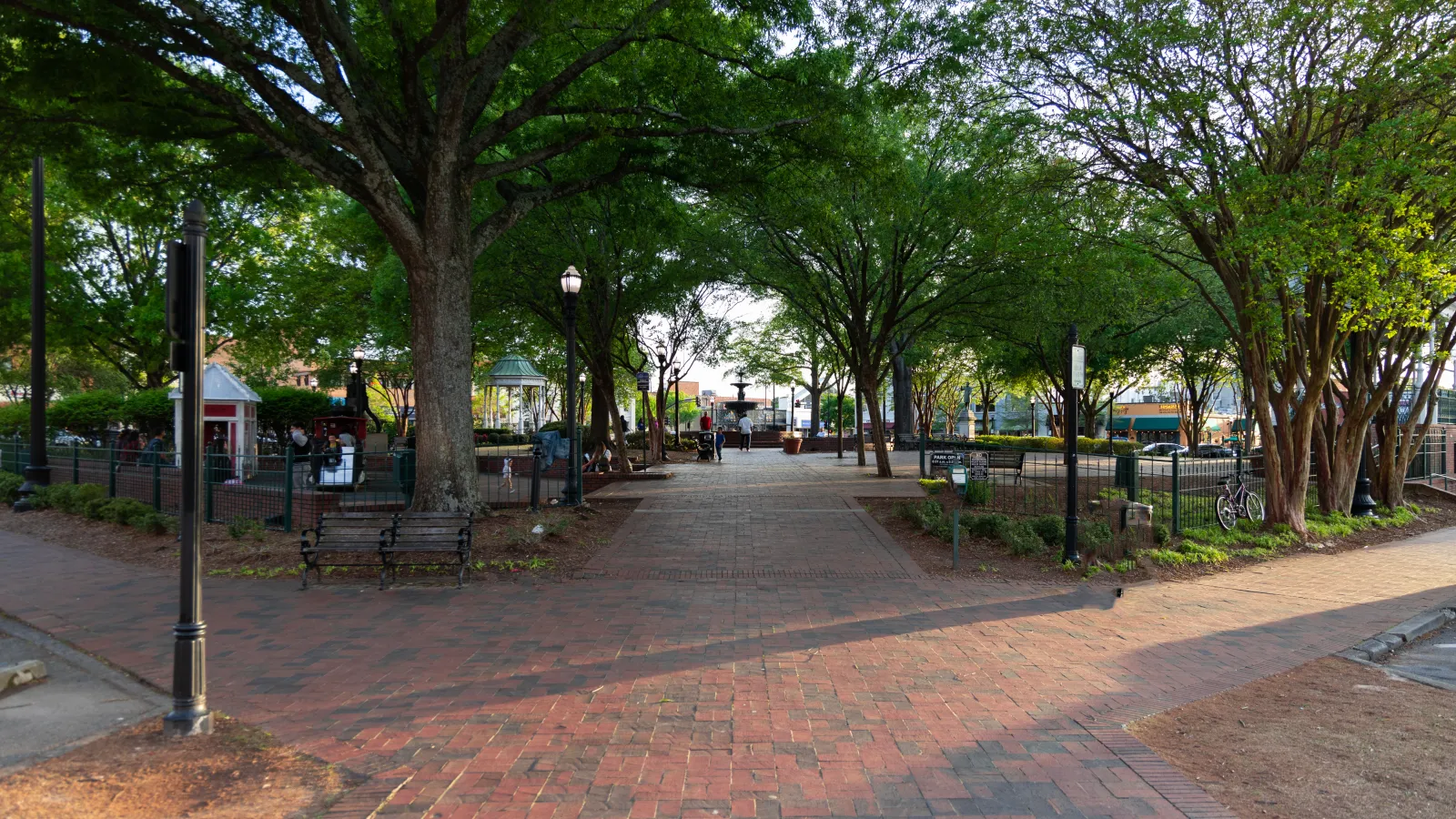 a brick walkway with trees and benches with Pearl Street Mall in the background