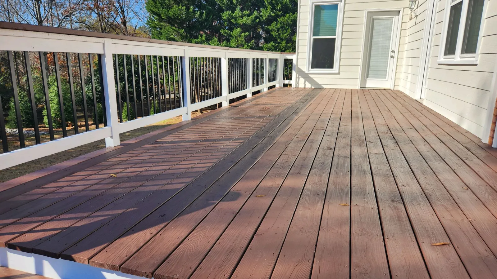 a deck with a wood railing and a house in the background