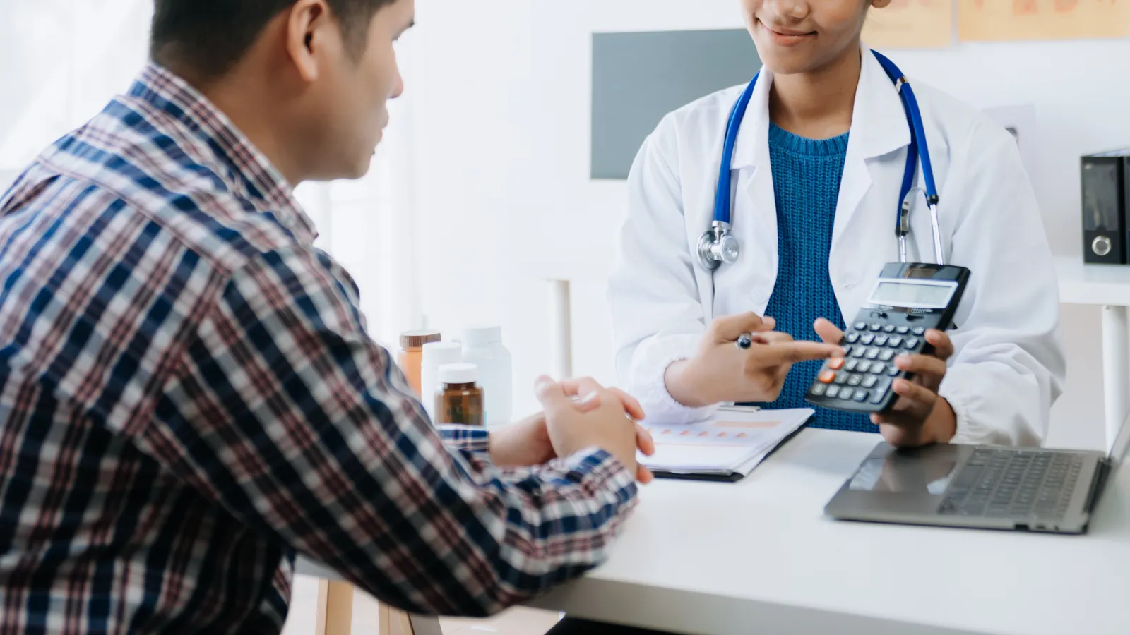 Doctor explaining medical costs to patient using a calculator in a clinic office setting.