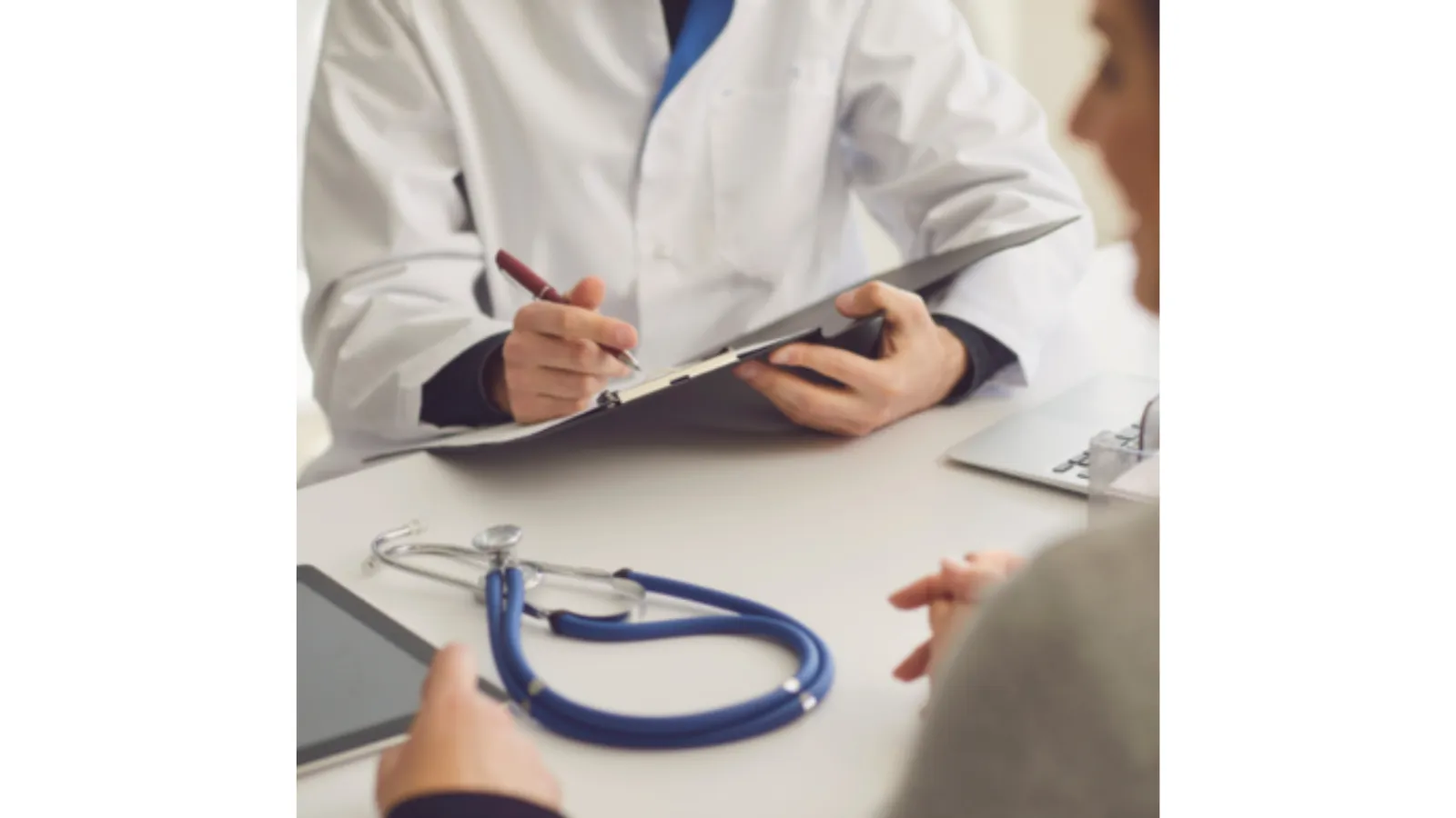A doctor reviews a clipboard while consulting with a patient, stethoscope on the table.