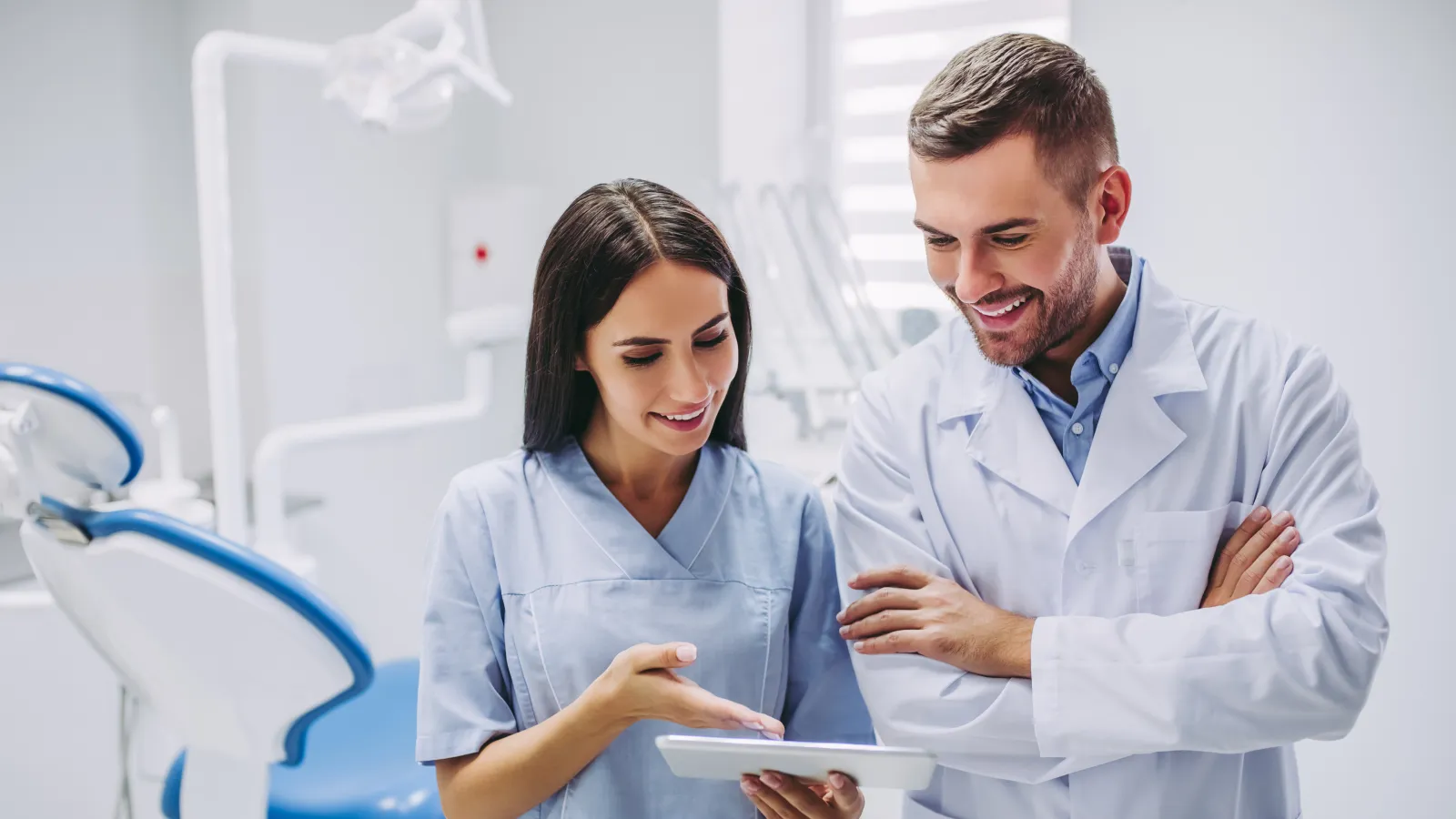 Male and female dentists in clinic reviewing patient information on a digital tablet together.