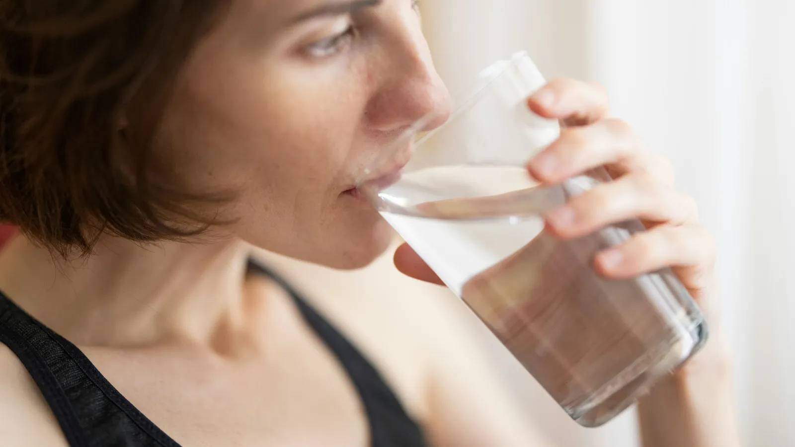 Close-up of a woman drinking a glass of water indoors, focusing on her face and hand holding the glass.