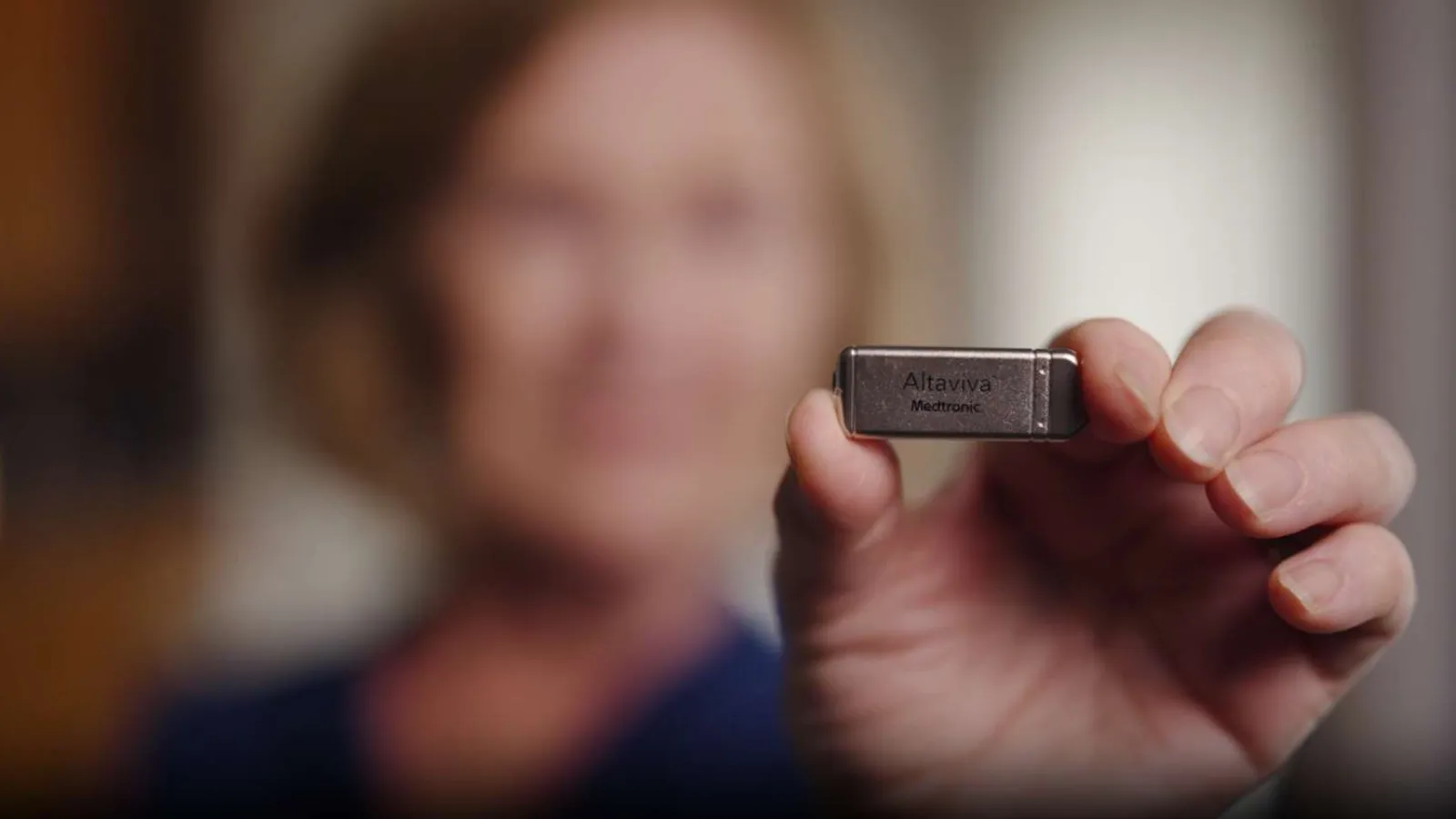 Person holding a small metallic Altaviva Medtronic device with blurred background.