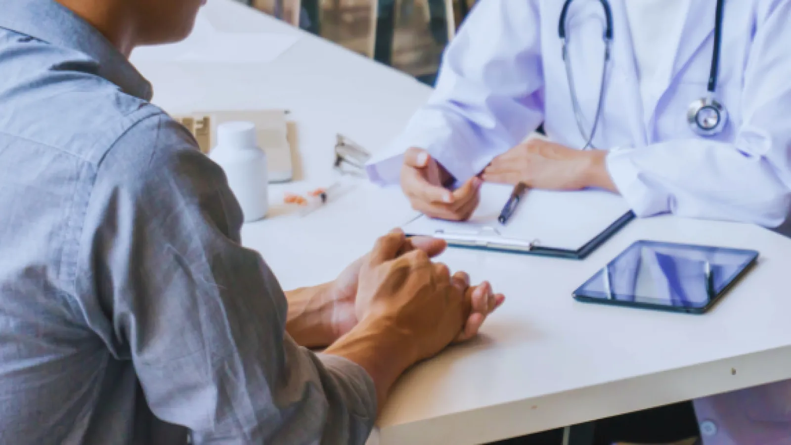 Doctor consulting patient with stethoscope, clipboard, and medical supplies on table during appointment
