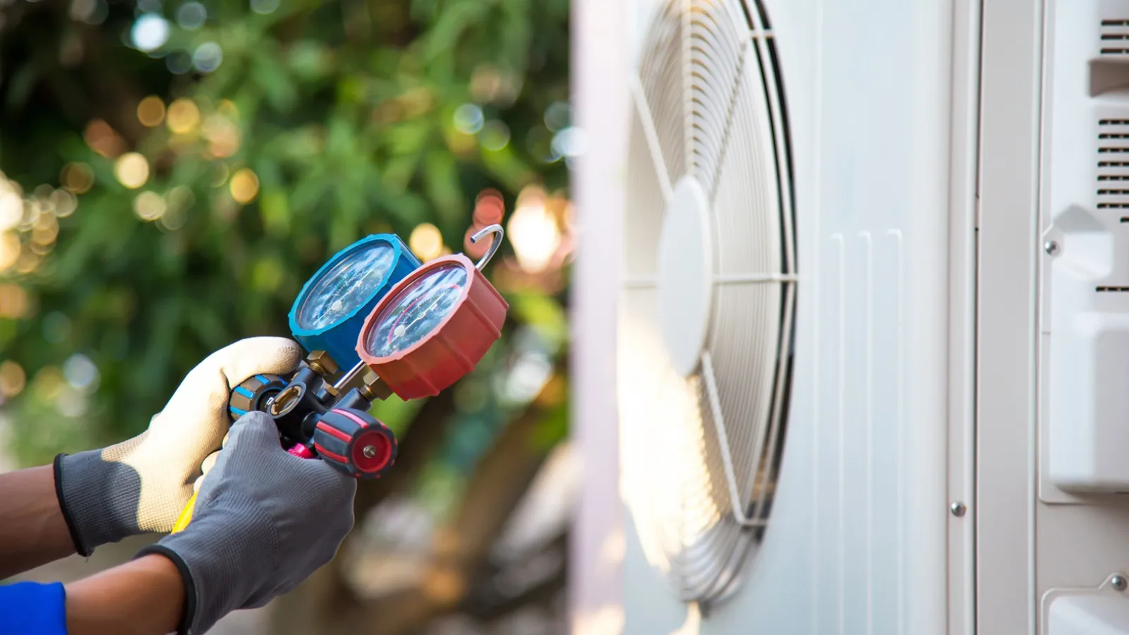 Technician wearing gloves using pressure gauges to service an outdoor air conditioning unit during maintenance.