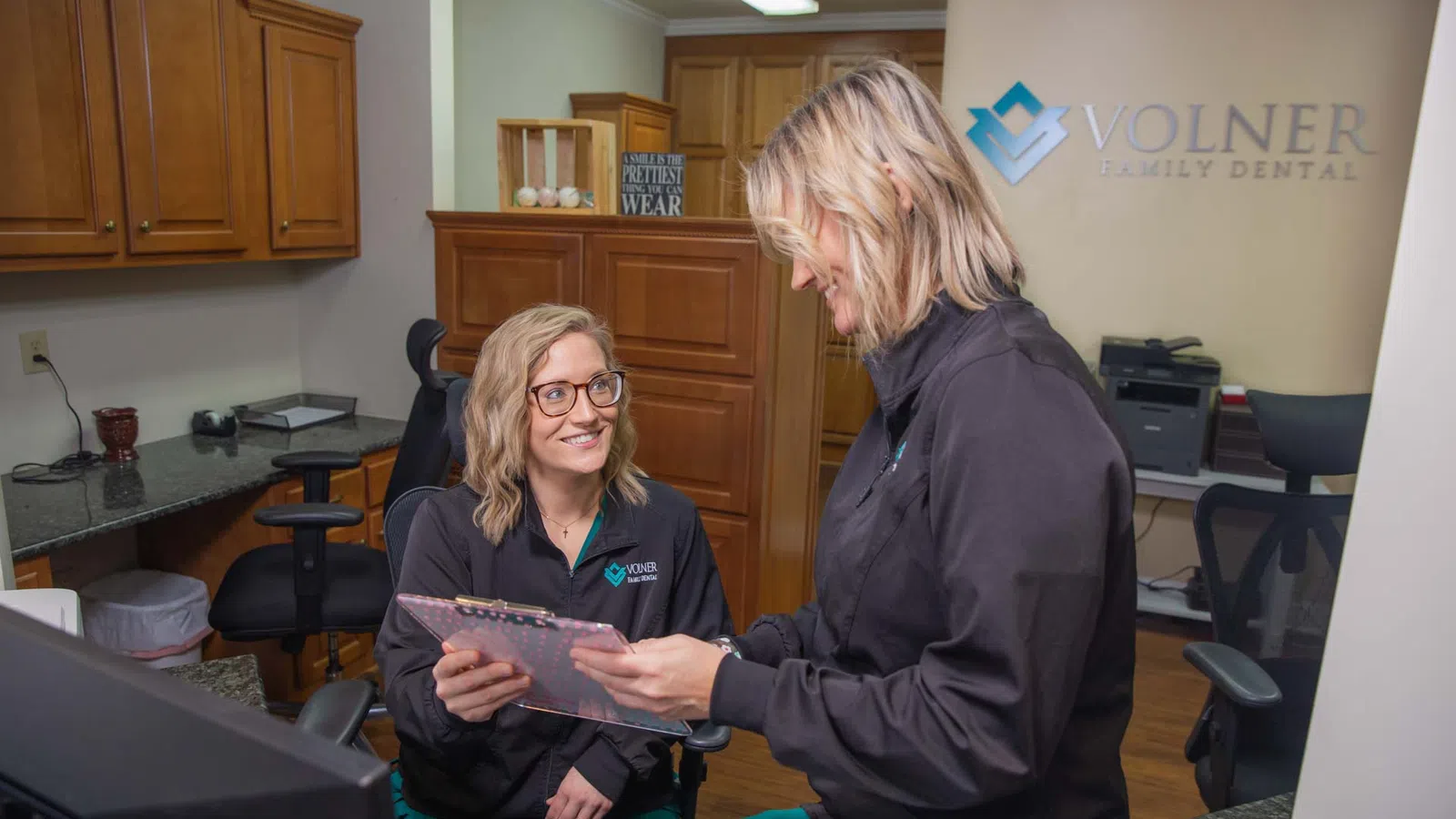 Two dental professionals in black jackets discussing patient information at Volner Family Dental office.
