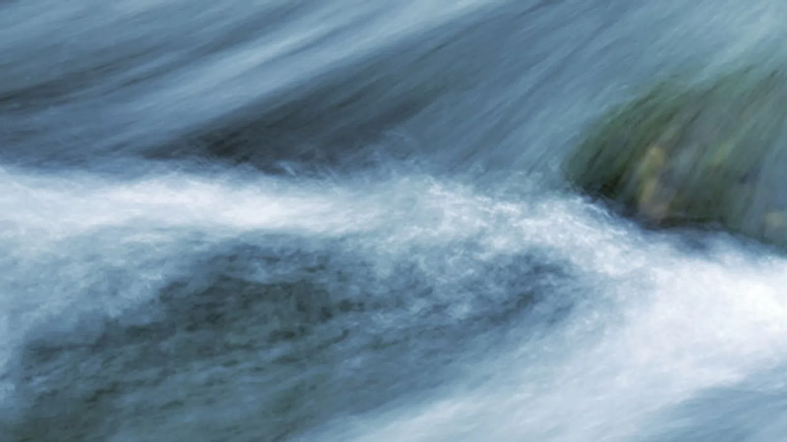Smooth flowing water cascading over rocks in a stream, creating a misty, serene effect in natural light.