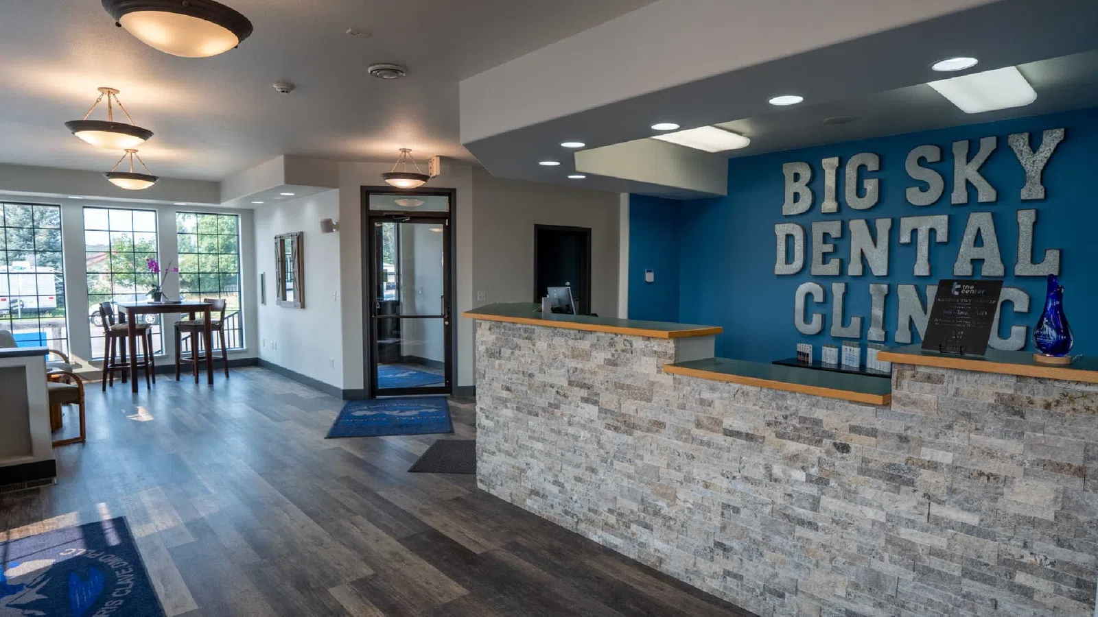 Reception area of Big Sky Dental Clinic with stone desk, blue wall, seating, and natural light from large windows