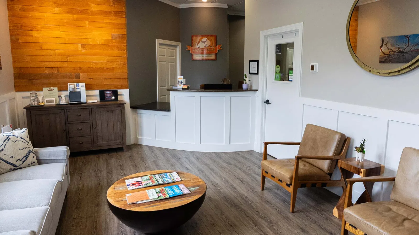 Cozy modern waiting room with wooden floor, beige leather chairs, sofa, round coffee table, and reception desk.
