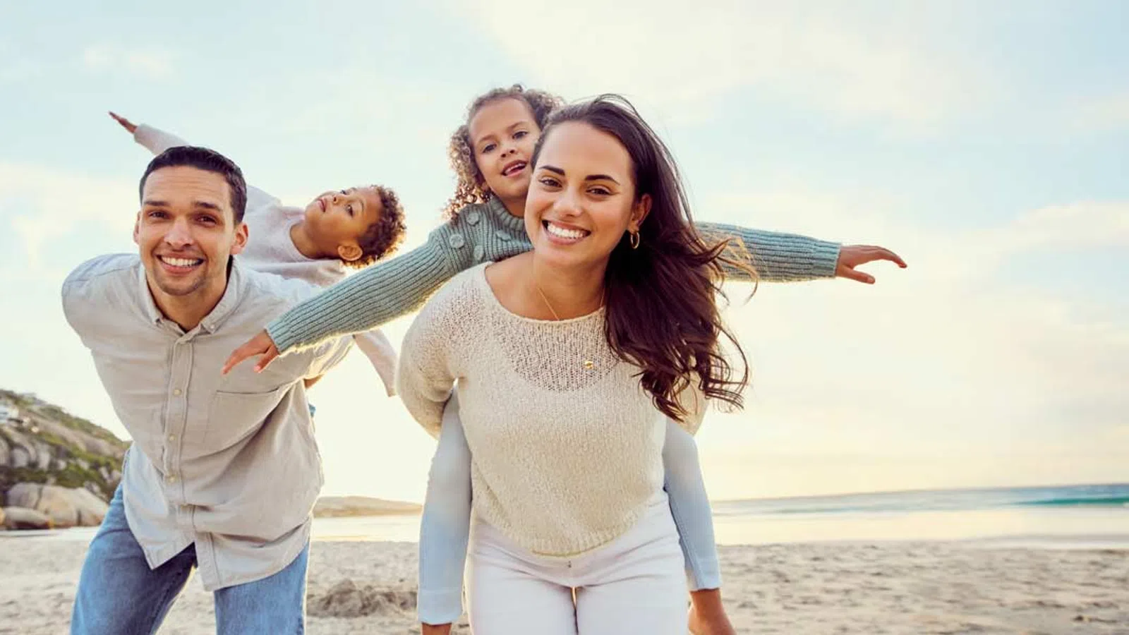 Happy family of four playing and smiling on a sunny beach with ocean and sky background