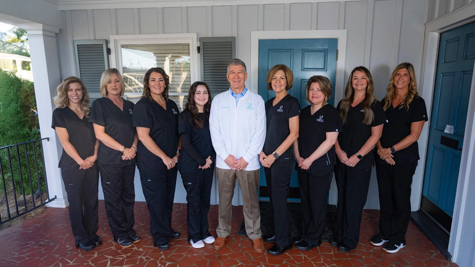 Medical team posing outdoors in front of a building wearing black scrubs and a white coat.