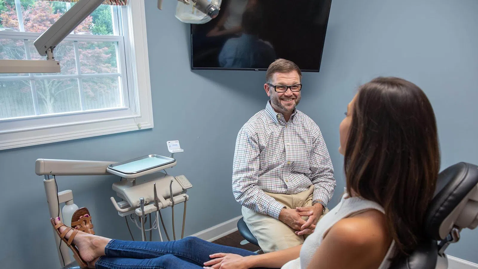 Dentist consulting a female patient in a modern dental office with dental equipment and window natural light