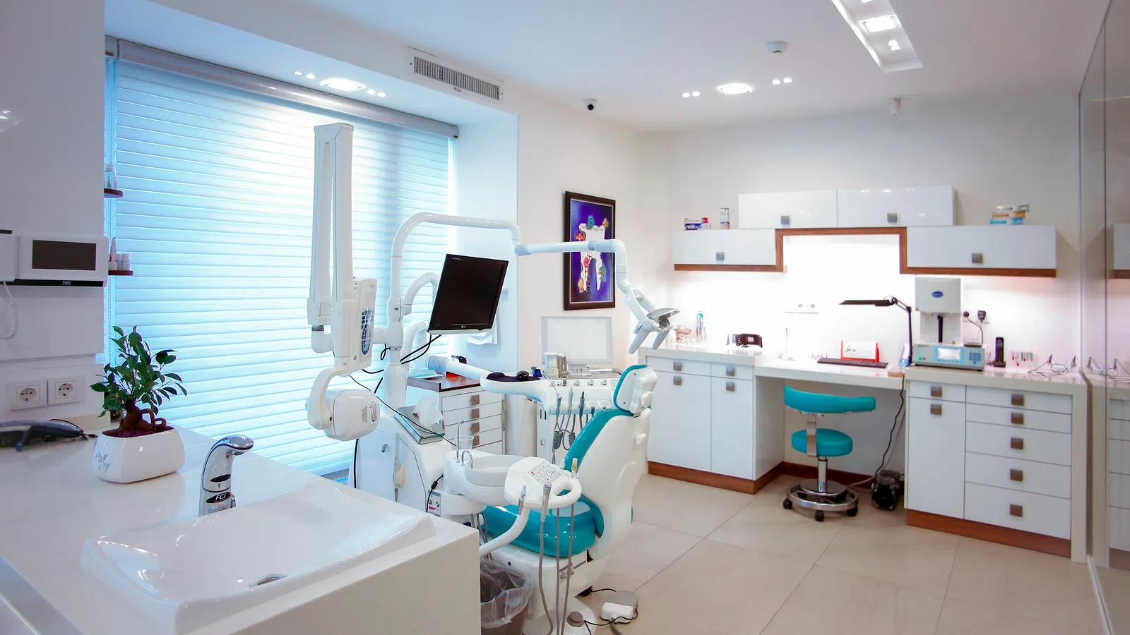 Bright modern dental clinic with white cabinets, dental chair, equipment, and clean workspace under natural light.