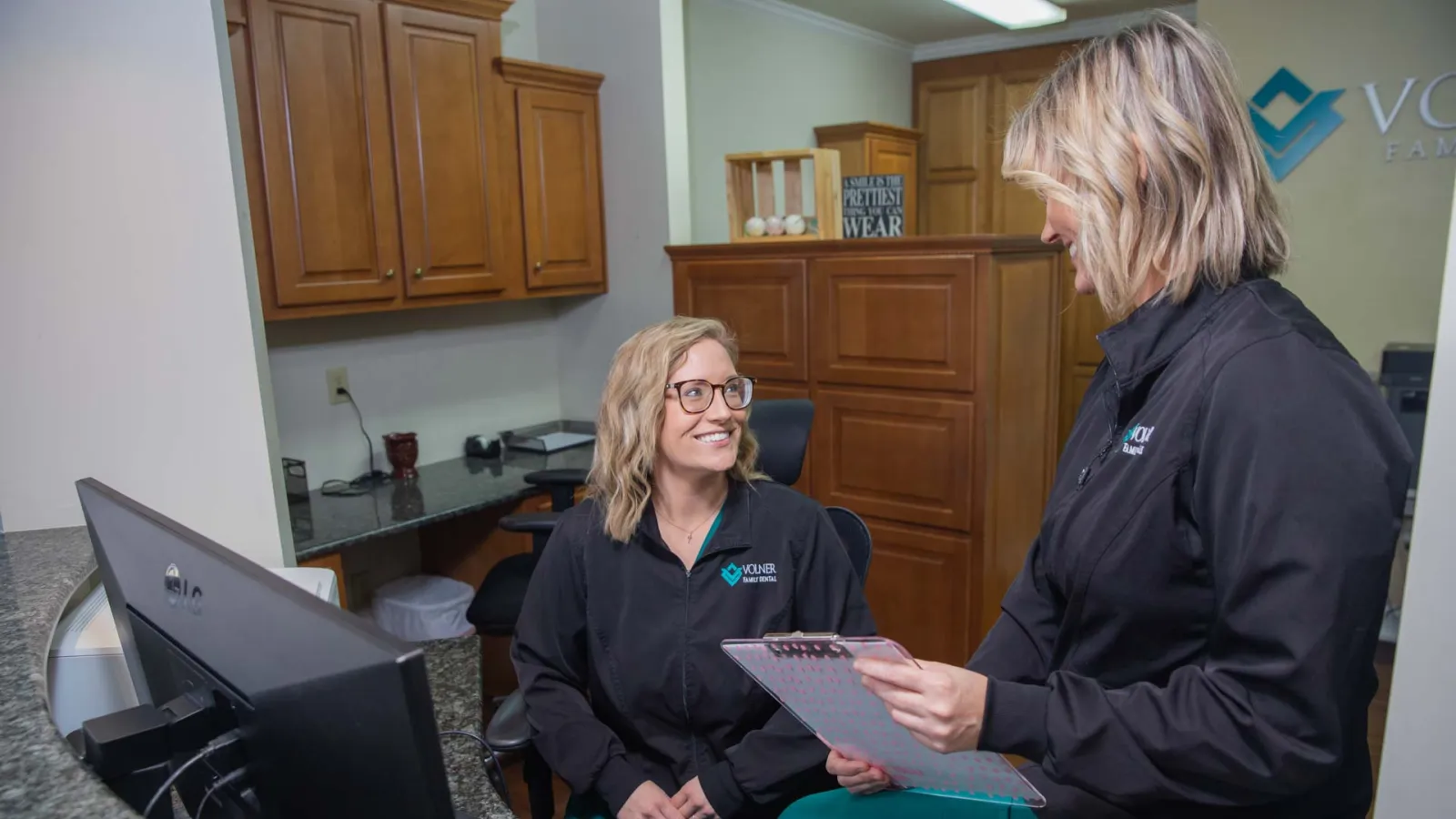 Two female medical professionals in black jackets discussing patient files in a modern clinic office.