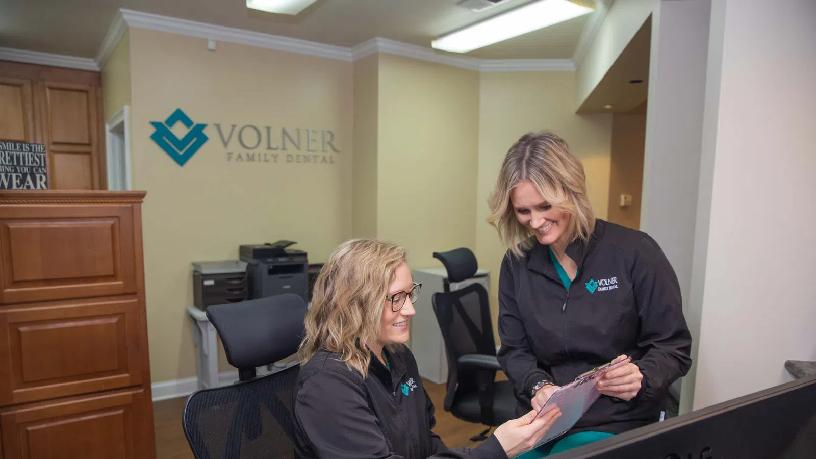 Two female dental staff members reviewing a chart in Volner Family Dental office with logo in background