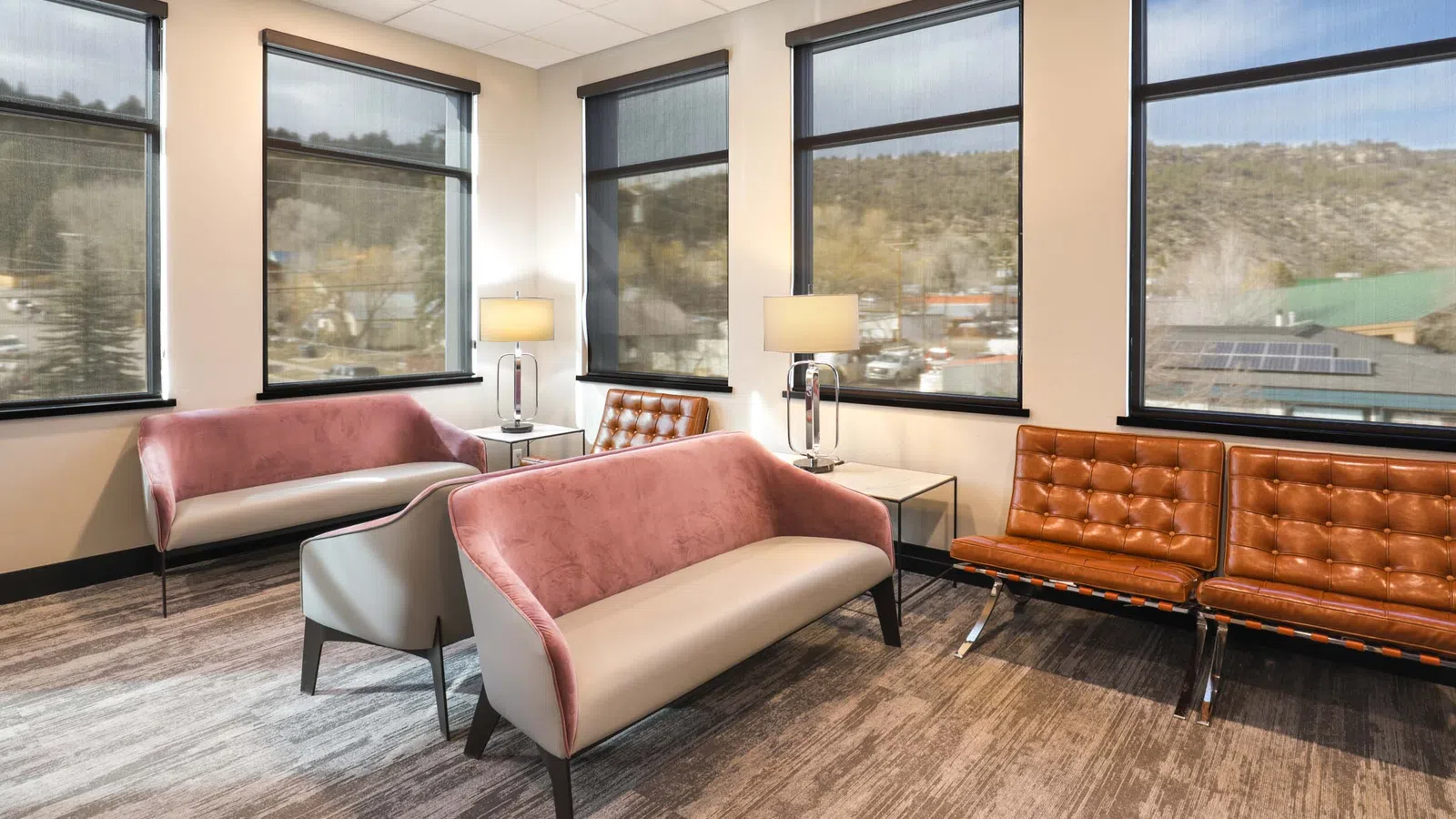 Modern office waiting room with pink and brown leather sofas, large windows, and natural lighting.
