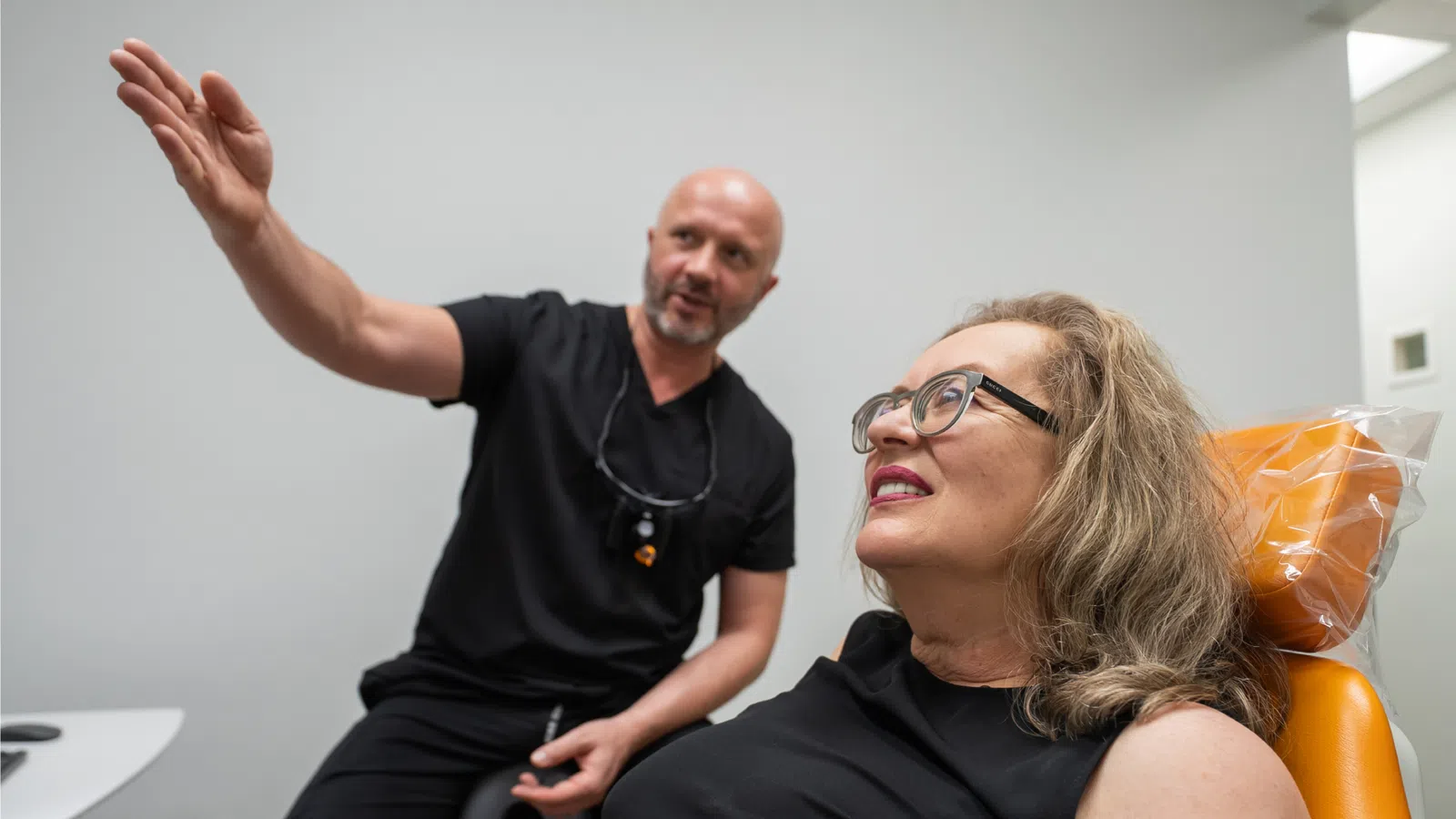Dentist explaining treatment to woman patient sitting in dental chair with orange headrest in clinic