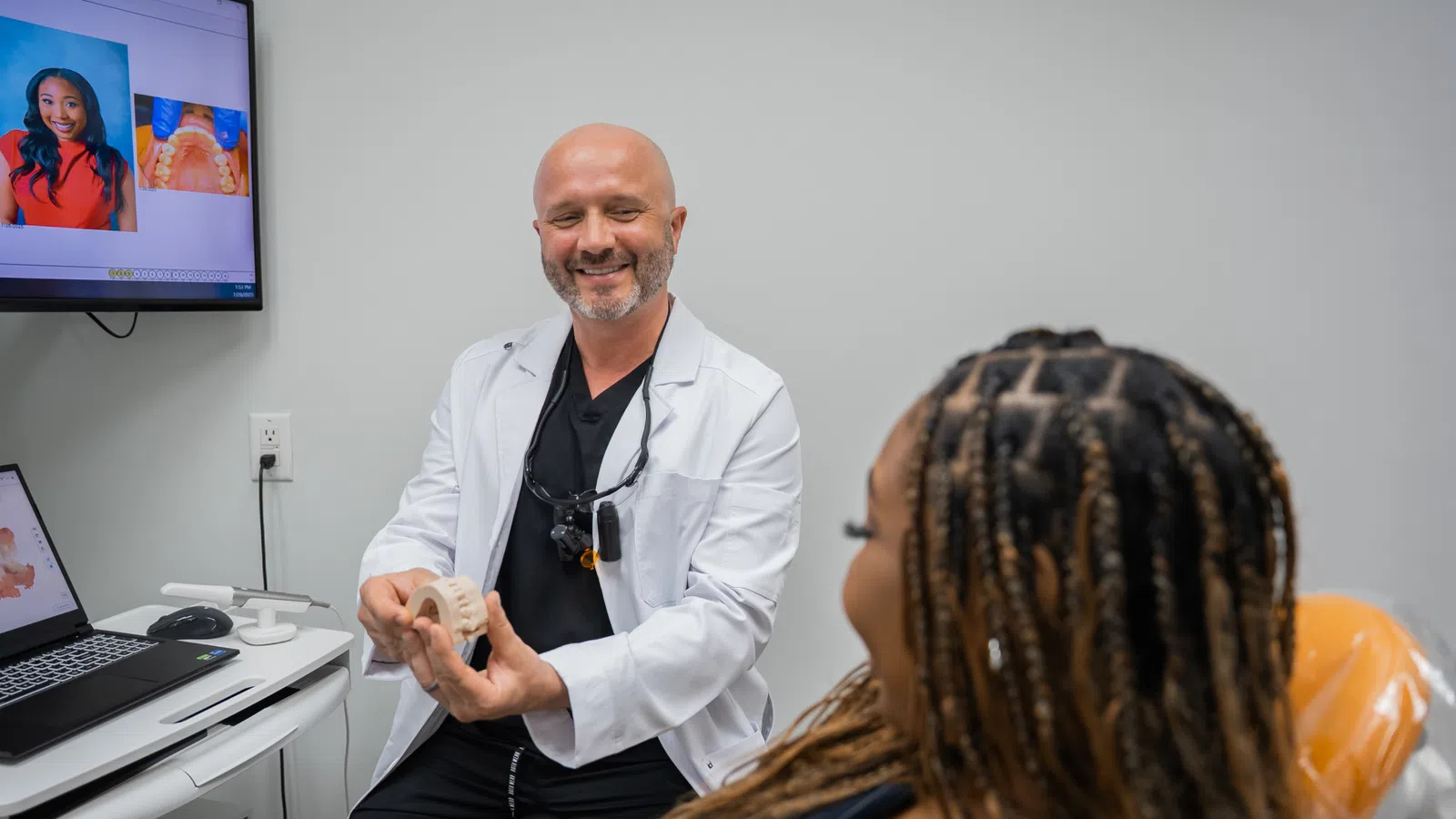 Dentist explaining dental model to patient in modern clinic with dental images on screen