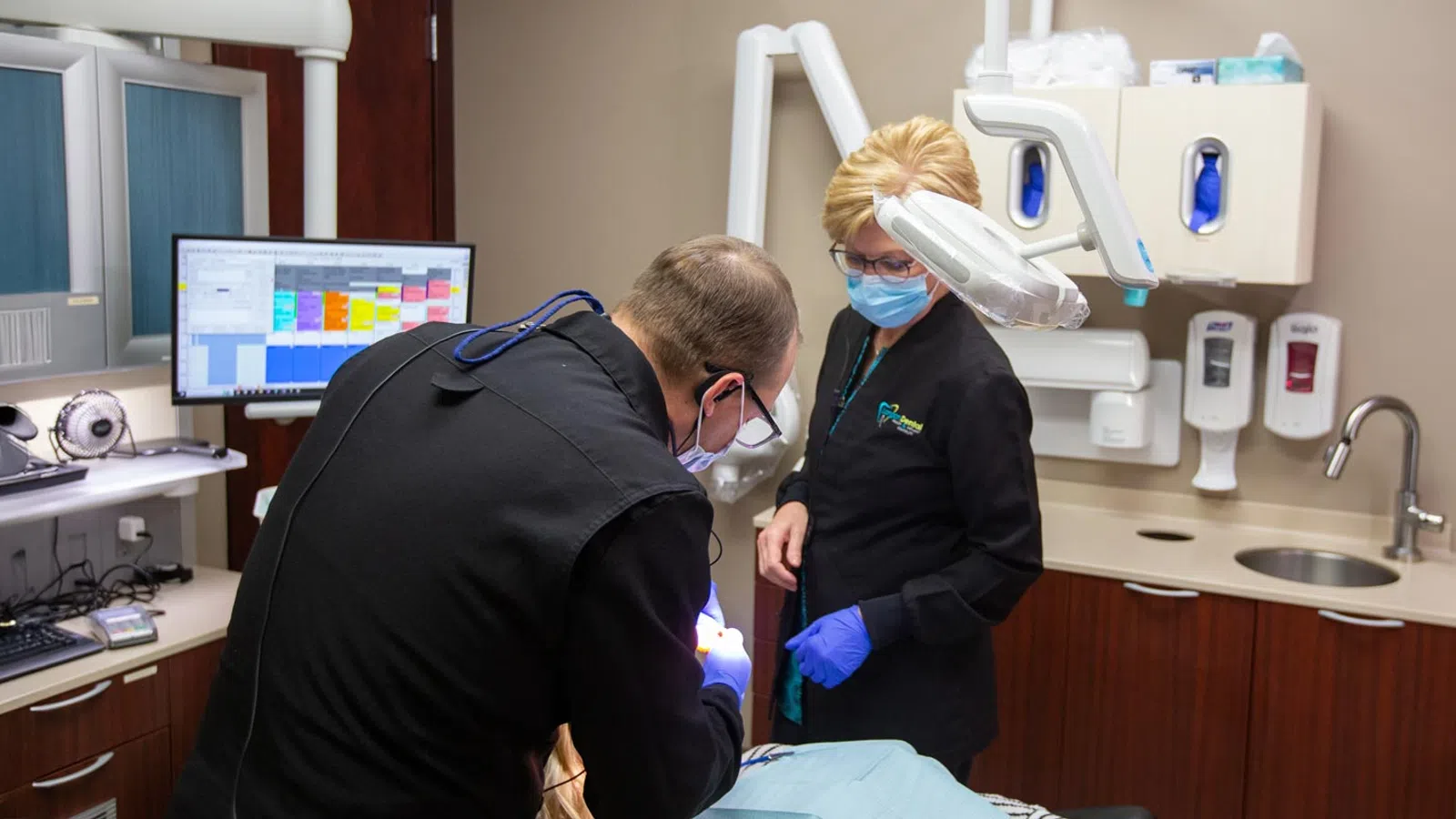 Dental professionals in a modern clinic, performing a procedure with high-tech equipment and PPE.