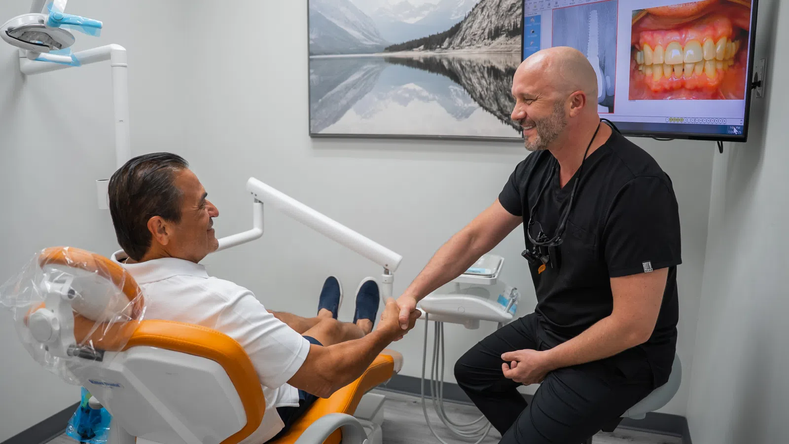 Dentist shaking hands with patient in a modern dental clinic with teeth images on a screen