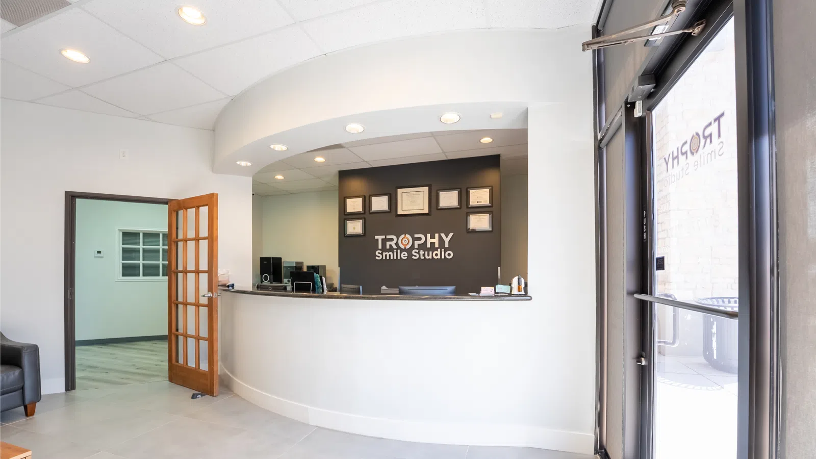 Bright dental office reception area with curved white desk and Trophy Smile Studio logo on black wall