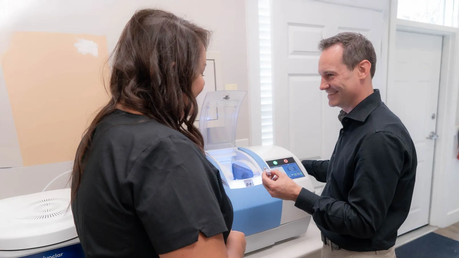 Dentists operating advanced dental equipment in clinic with patient and technician discussing procedure.