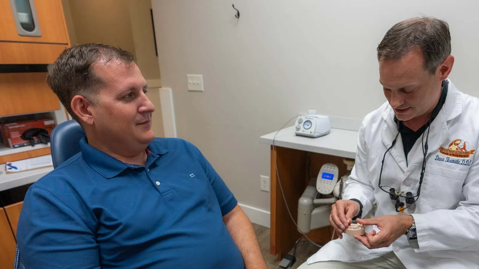 Dentist explaining dental treatment to patient using a dental model in a clinic room.