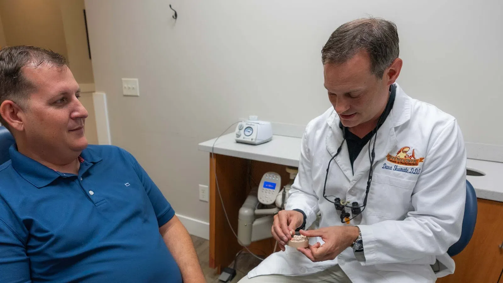 Dentist explaining a dental model to a patient in a modern clinic setting during consultation.