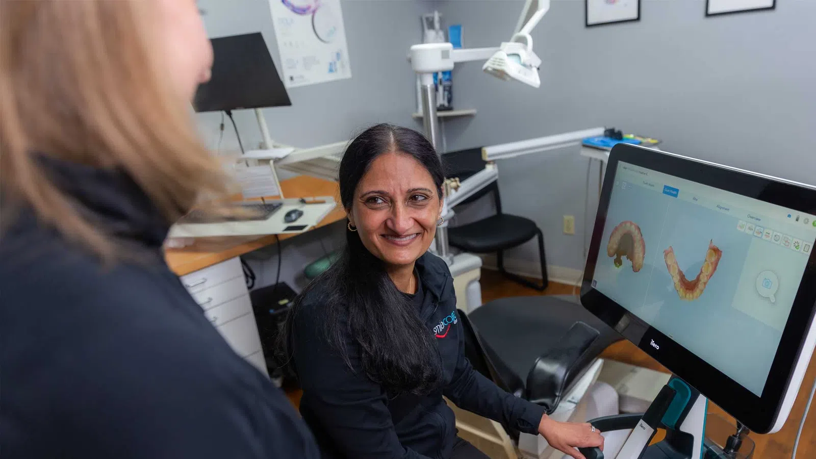 Female dental professional using digital scanner with 3D teeth images on screen in clinic setting