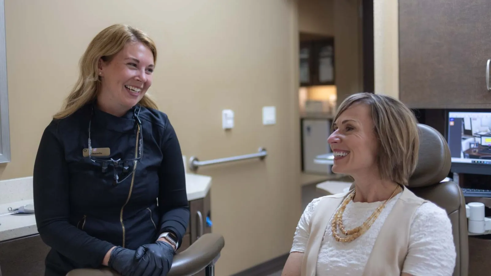 Dentist and patient smiling and conversing in a modern dental office during a consultation appointment.