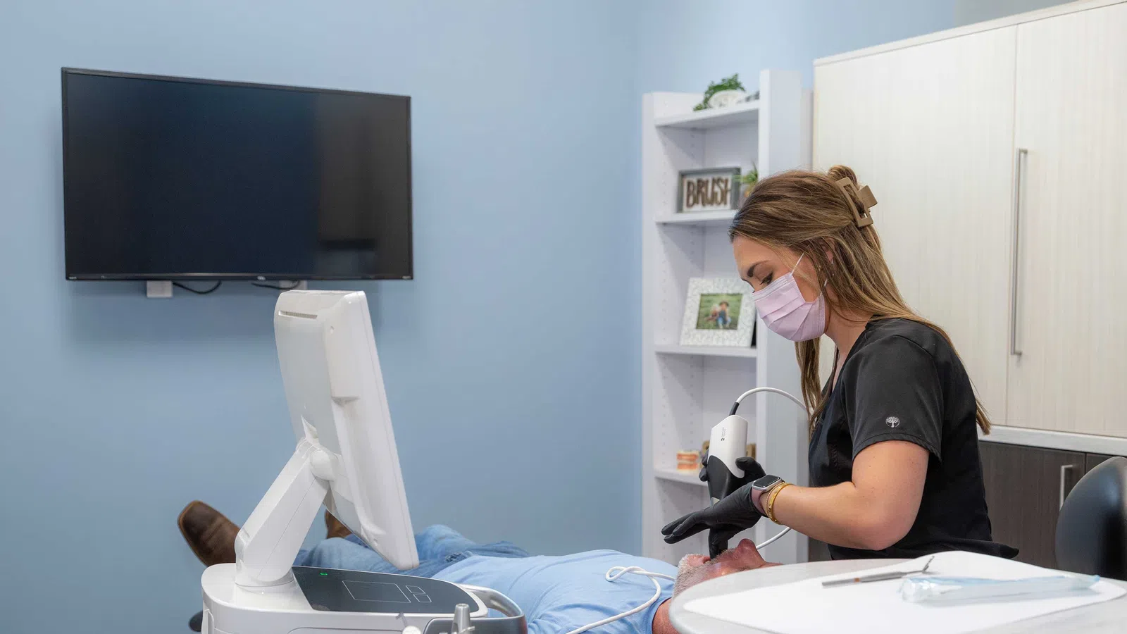 Dental professional wearing mask treating patient using advanced dental equipment in modern clinic room.