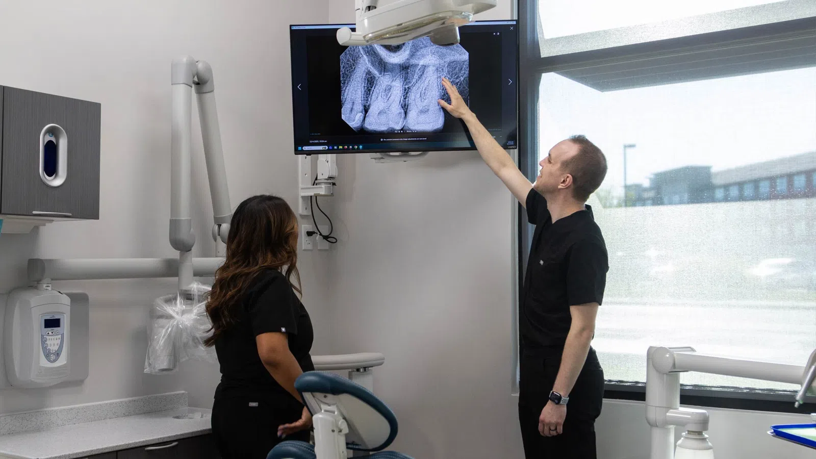 Dentists examining a digital dental X-ray on a screen inside a modern dental clinic room.
